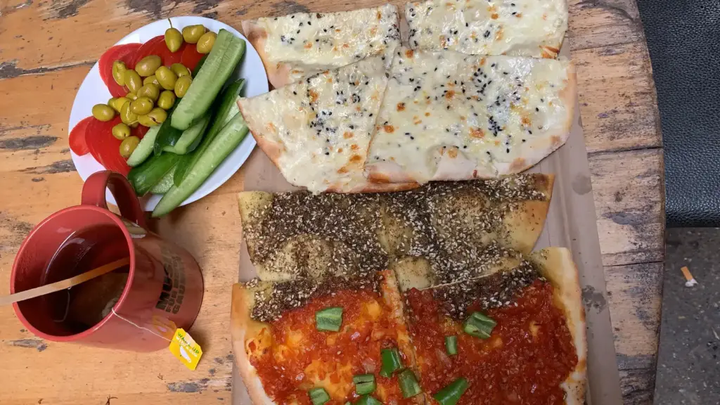 Manakish mit Beilagen Fladenbrote mit Zaatar, Käse und Tomate, dazu Gurken und Oliven
